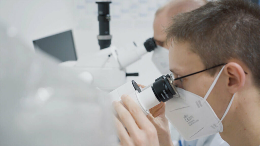 Person mit medizinischer Maske schaut durch Mikroskop